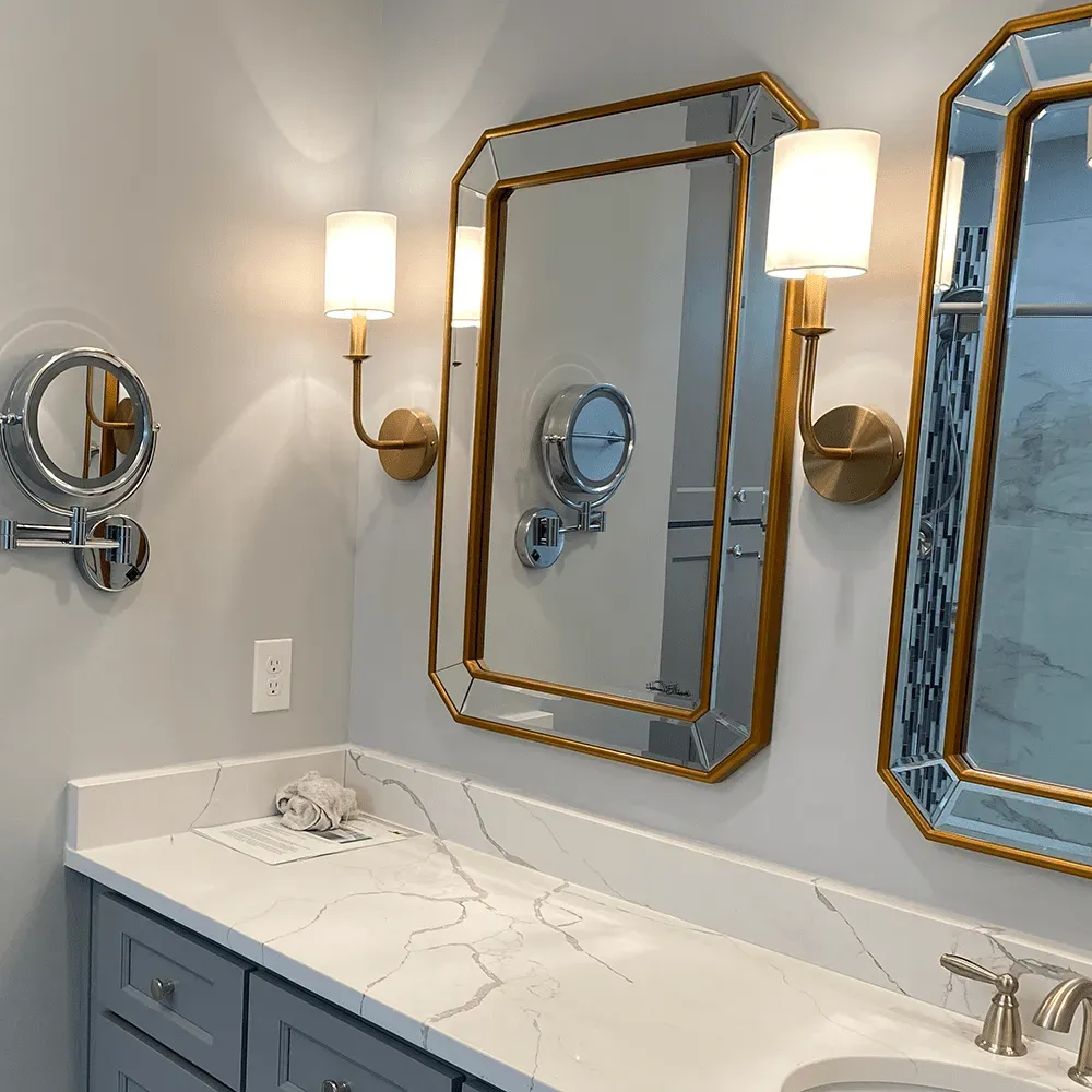 A bathroom with gray cabinets, white and gray marbled countertop, double vanity sinks, and two large gold-framed mirrors.