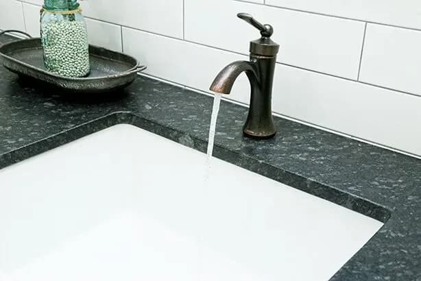 A close-up of a bathroom sink with dark-colored countertop and brushed brass fixtures.