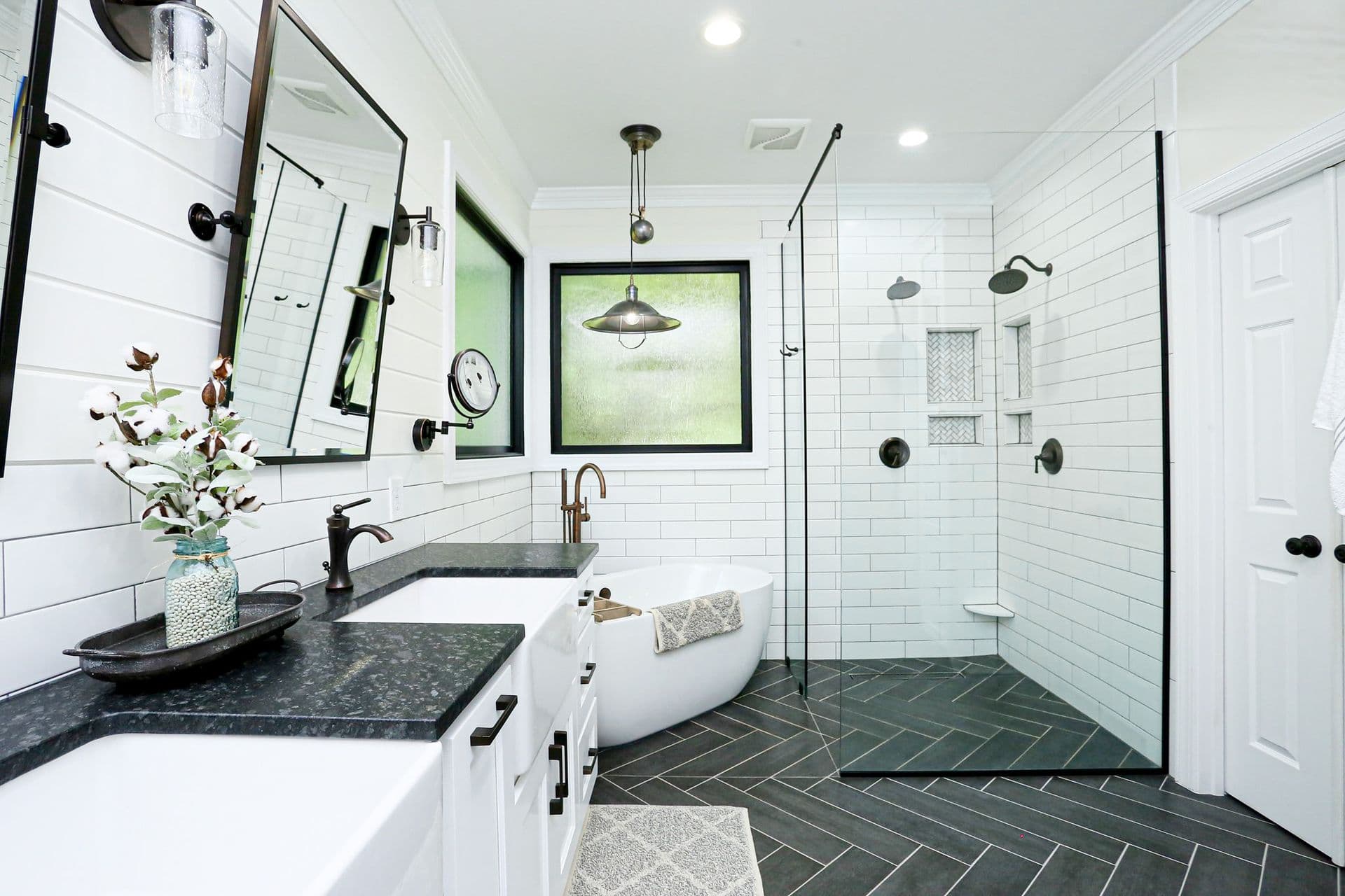 A bathroom with dark countertops, white cabinets, black fixtures, large soaking tub, and glass walk-in shower with dark tile floor.