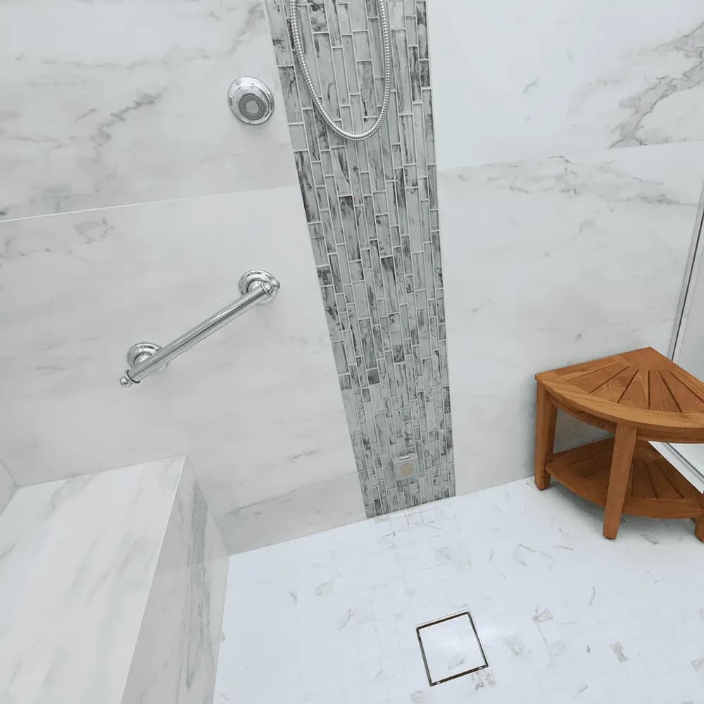 A walk-in shower with white and gray marbled walls, mosaic gray tile accent, grab bar, and built-in bench.