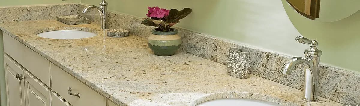 Close-up of double vanity sinks in a bathroom with beige cabinets and marbled countertop.