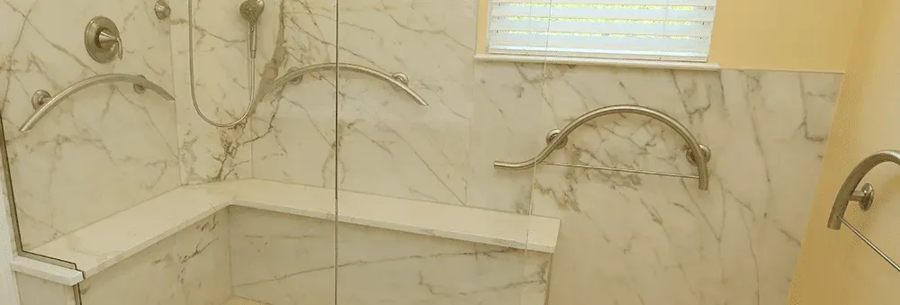 A walk-in shower with marbled walls, built-in bench, and multiple curved grab bars.