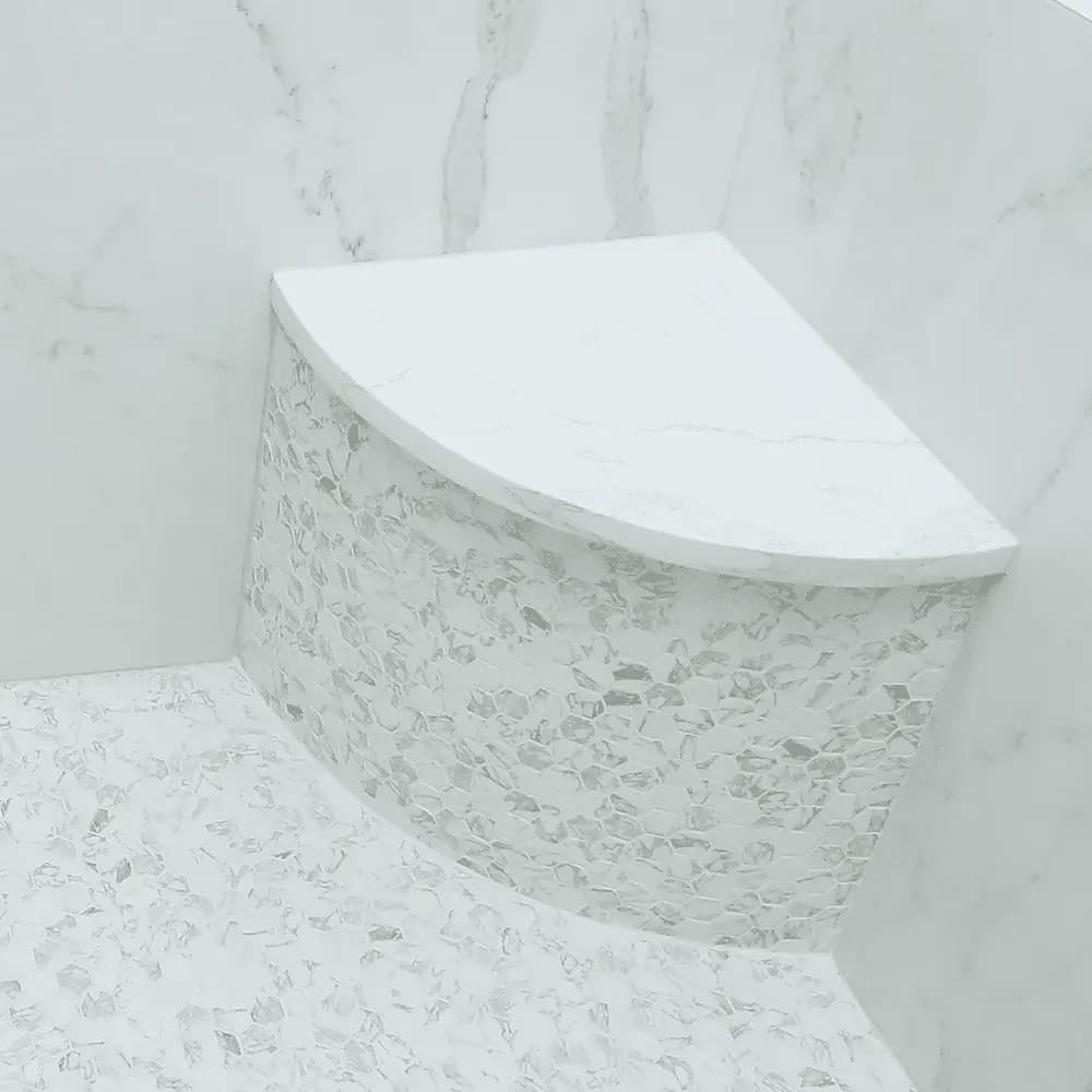 A close-up of a built-in, rounded corner stone bench in a walk-in shower.