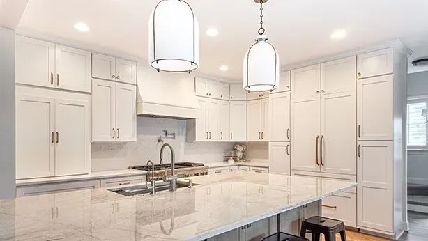 A kitchen with white cabinets and gold-colored fixtures, large central island with gray cabinets and white and gray marbled countertop.