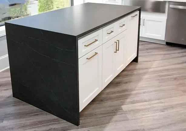 A kitchen island with black marbled countertop and white cabinets with gold-colored fixtures.