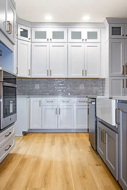 A kitchen with white cabinets, gray tile backsplash, gray island, and vinyl plank flooring.