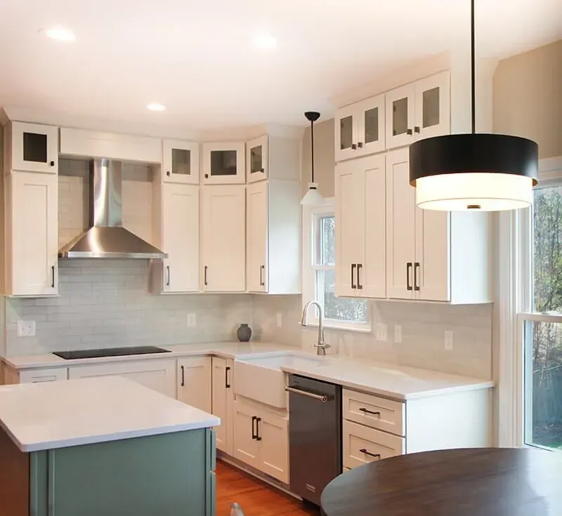 A kitchen with white cabinets, white subway tile backsplash, black fixtures, white countertops, and a central island with a green base.
