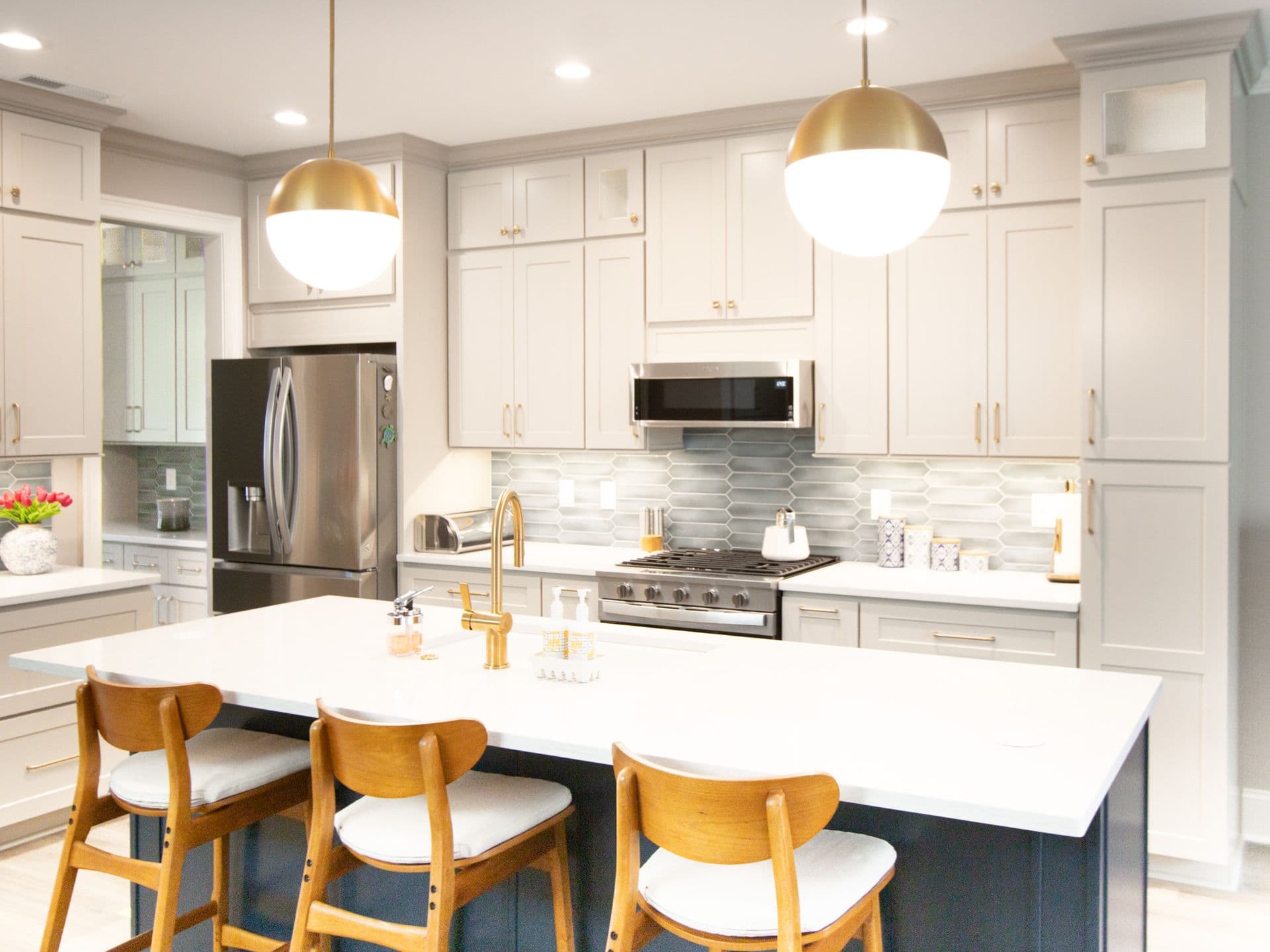 A kitchen with white cabinets, gold fixtures, central island with dark blue base and white countertop, and geometric tile backsplash.