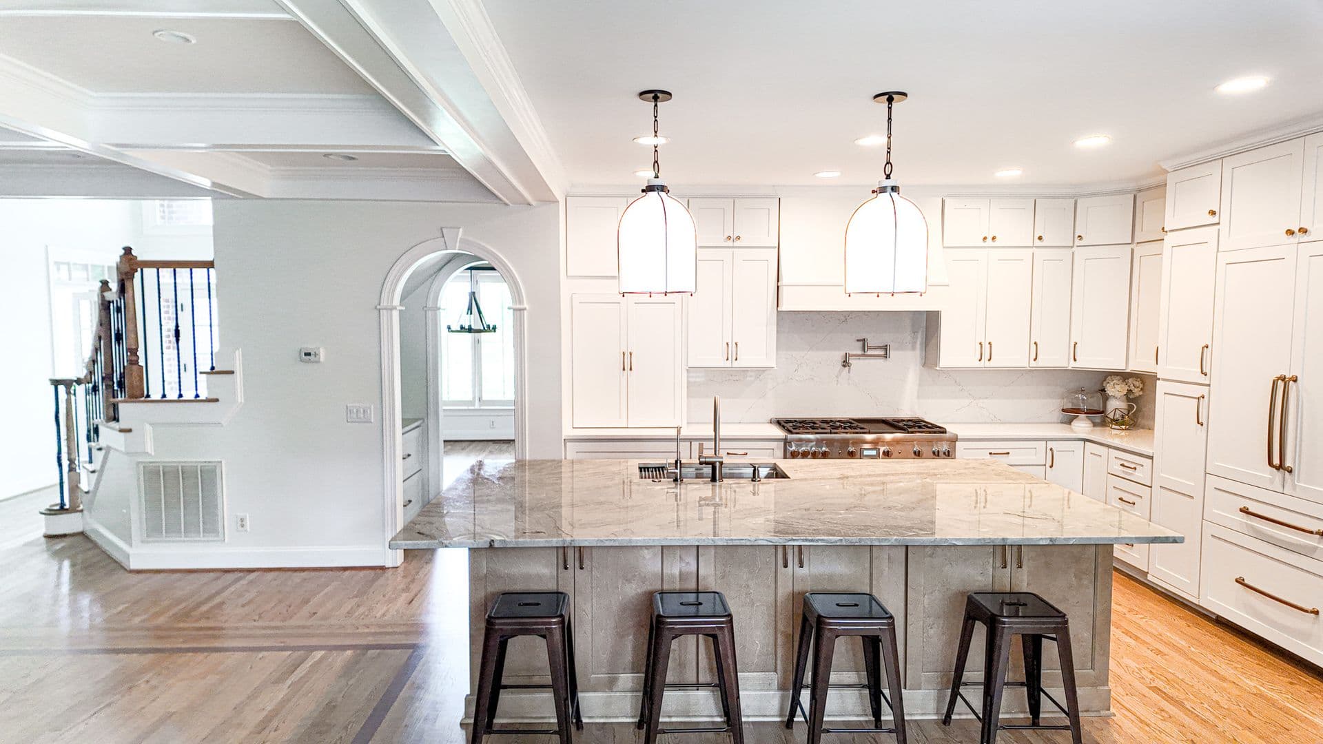 A white kitchen with white cabinets, large central gray stone island, and bar stool seating.