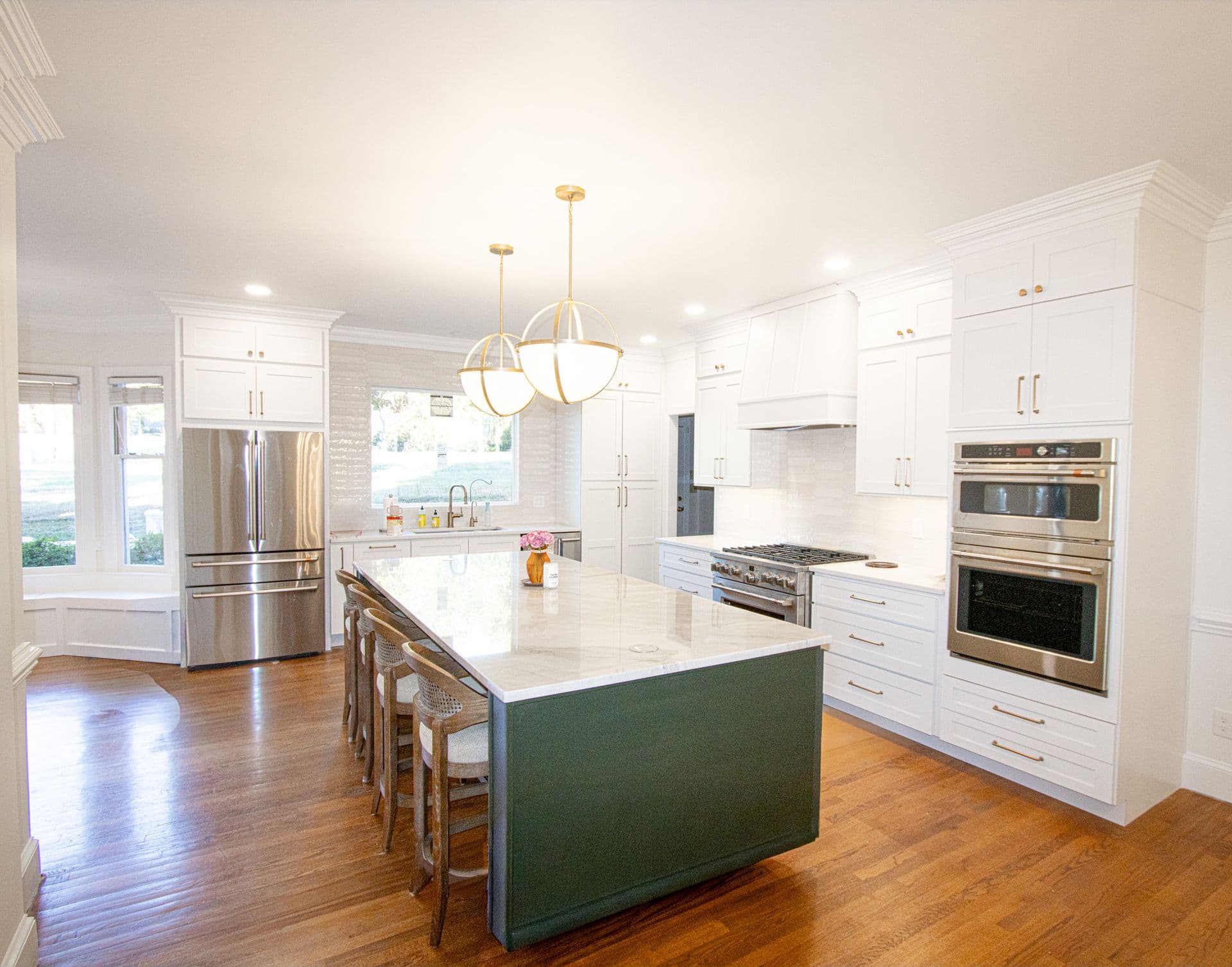 A kitchen with white cabinets, white geometric tile backsplash, gold fixtures, white countertops, and a central island with a green base.